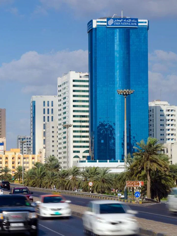 برج مكاتب زجاجي أزرق بجانب طريق تصطف على جانبيه أشجار النخيل في الشارقة في يوم صافٍ